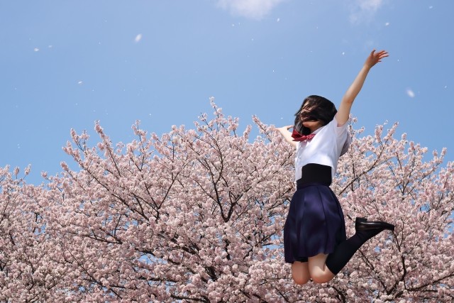 桜の前でジャンプする女子高生